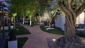 A landscaped garden with a paved walkway, trees, and white planters. - Camping Los Llanos (Denia)