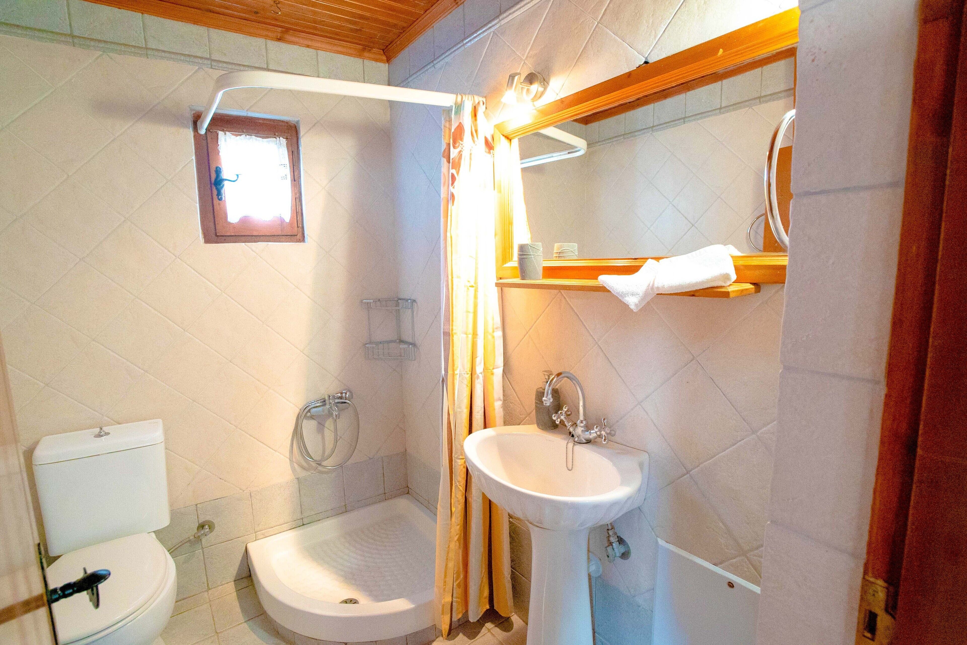 Ein Badezimmer mit Toilette, Dusche, Waschbecken und einem kleinen Fenster.