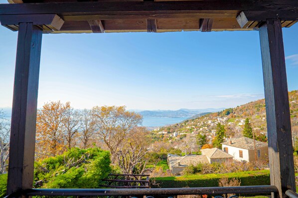 A wooden pergola structure with a view of a hillside village and a body of water in the distance. - Chrissi Nefeli (South Pelion)
