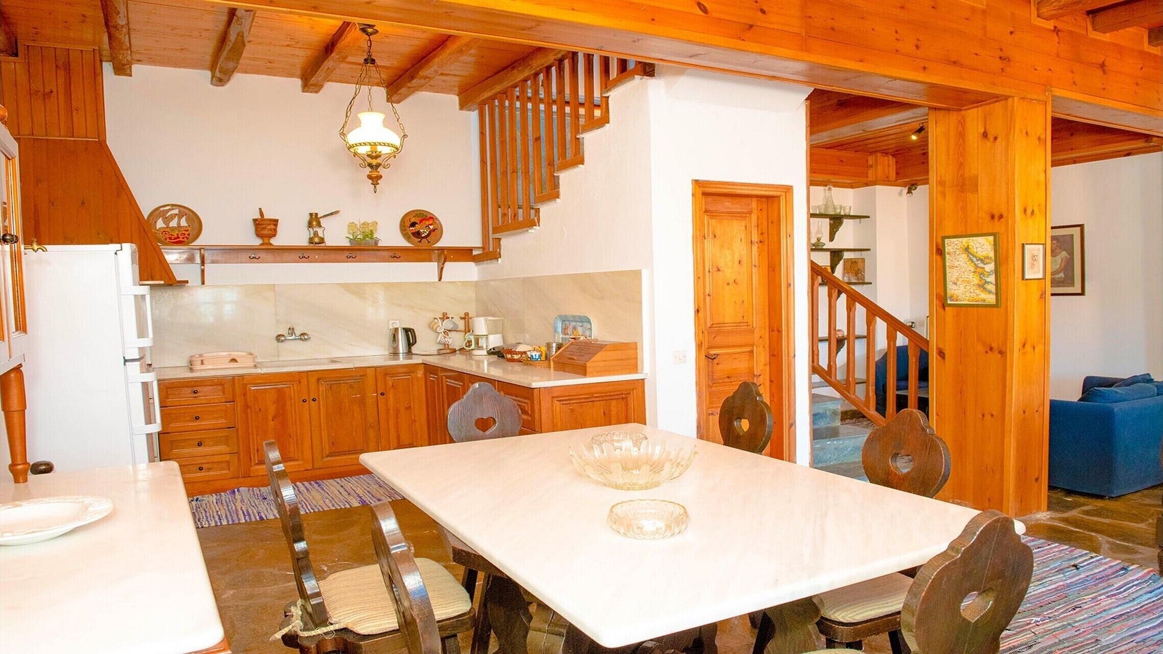 Una cocina acogedora con armarios de madera, encimera de mármol y una mesa de comedor con sillas. Una escalera conduce a otra habitación.