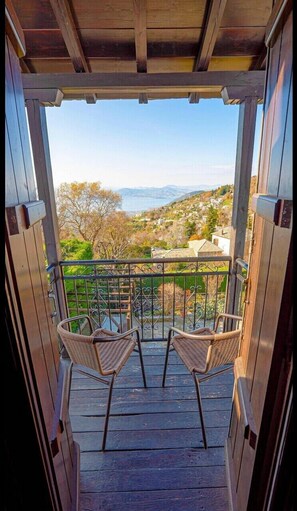 A wooden balcony with two wicker chairs facing a scenic view of a valley and a body of water. - Chrissi Nefeli (South Pelion)