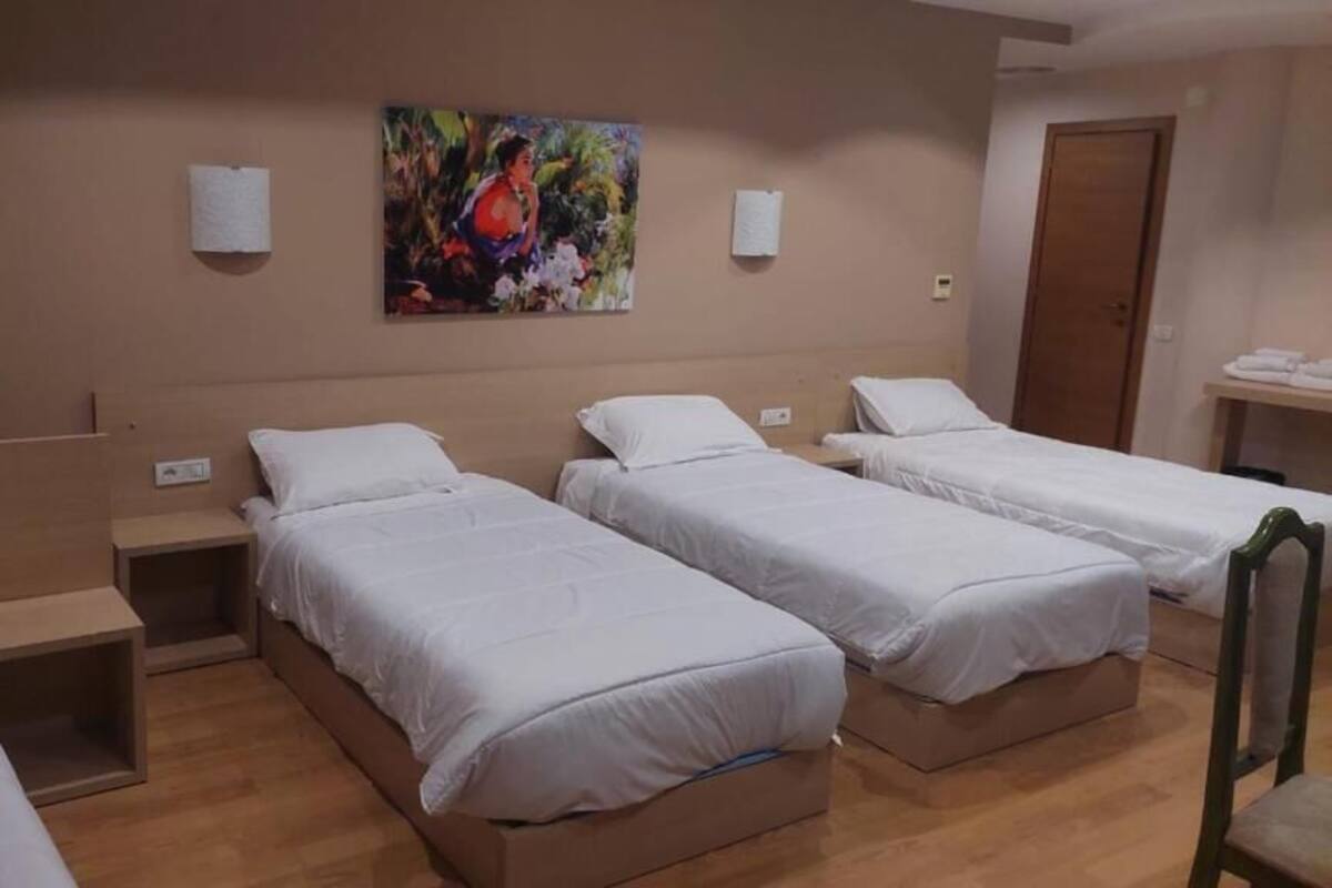 A hotel room with three single beds, a wooden floor, a painting on the wall, and a wooden door.