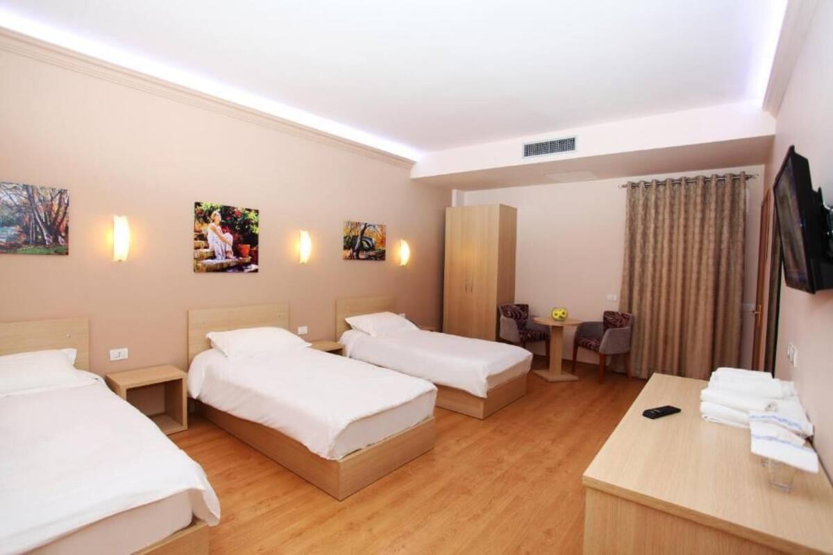 A hotel room with two single beds, a desk with a chair, a TV, and artwork on the walls.