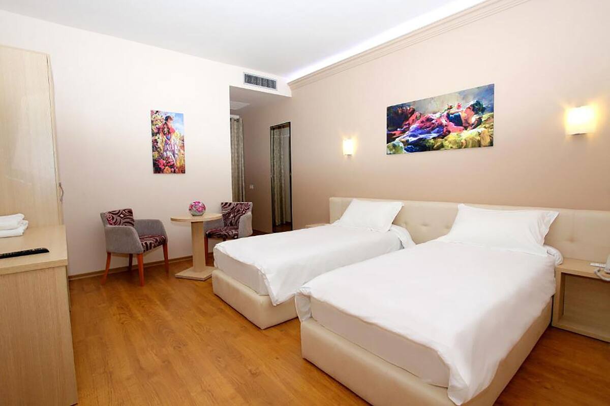 A hotel room with two beds, a desk, a chair, and artwork on the walls.