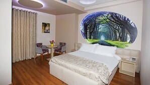 A hotel room with a bed, a small table with chairs, a nightstand, and a large forest-themed mural on the wall. - Hotel Green (Vaqarr)