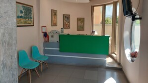 A reception area with a green desk, two turquoise chairs, and a flat-screen TV mounted on the wall. - Hotel Green (Vaqarr)