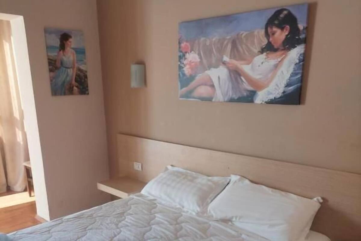 A bedroom with a bed, a nightstand, and two wall-mounted paintings.