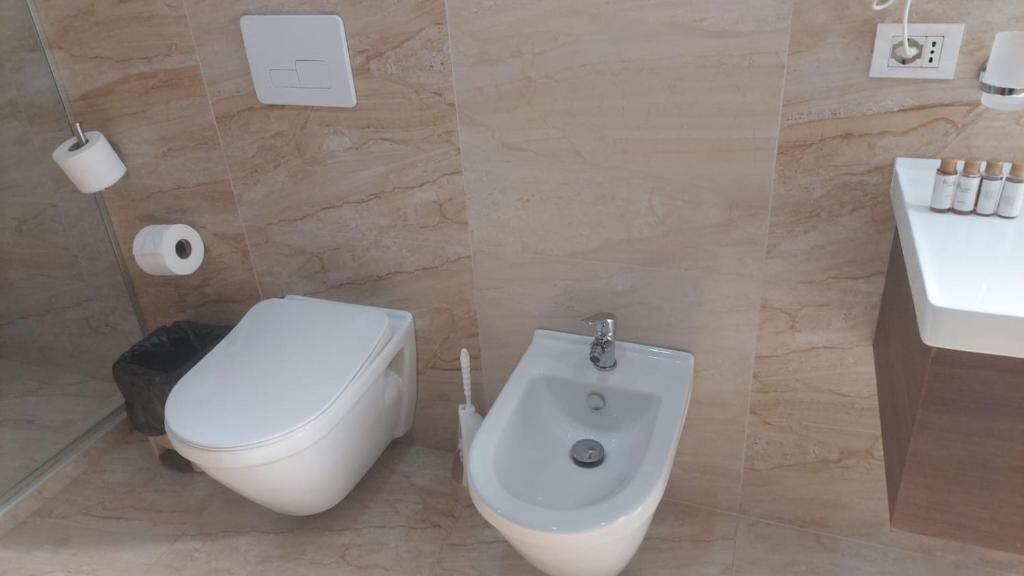 Kylpyhuone, jossa on bidee, wc-paperia ja pesuallas, jossa on hygieniatuotteita.