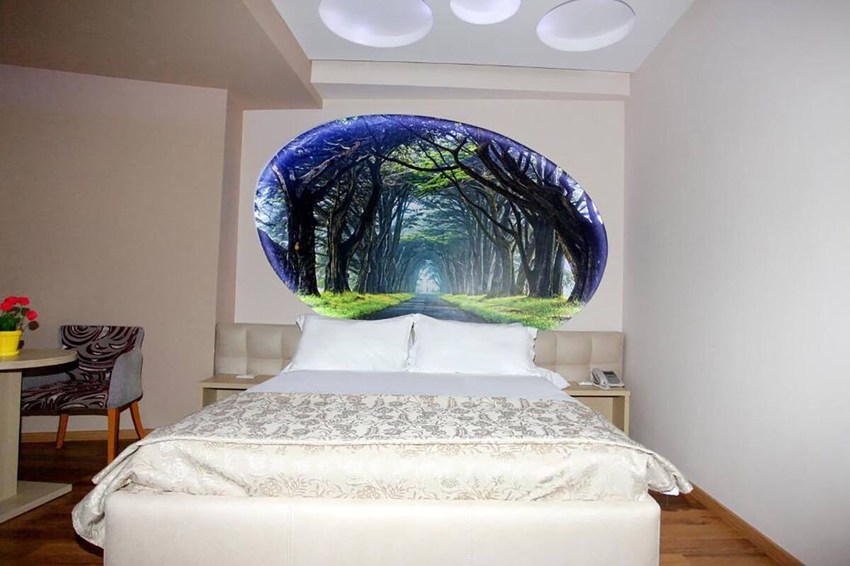 A bedroom with a bed, a nightstand, a chair, and a desk with a lamp.