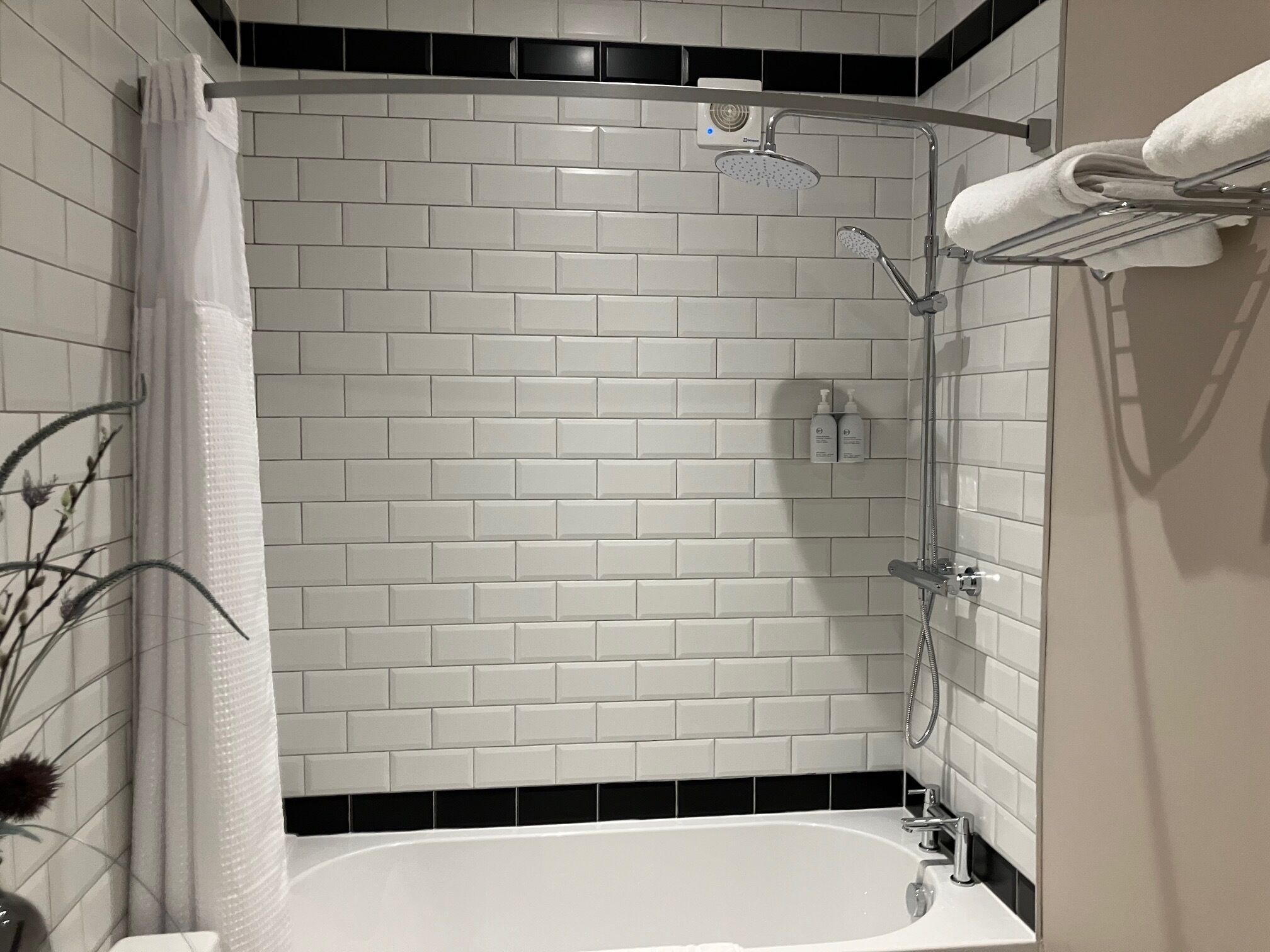 A modern bathroom with white subway tiles, a black-tiled shower area, a white bathtub, and a towel rack.