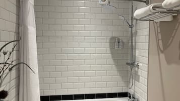 A modern bathroom with white subway tiles, a black-tiled shower area, a white bathtub, and a towel rack.