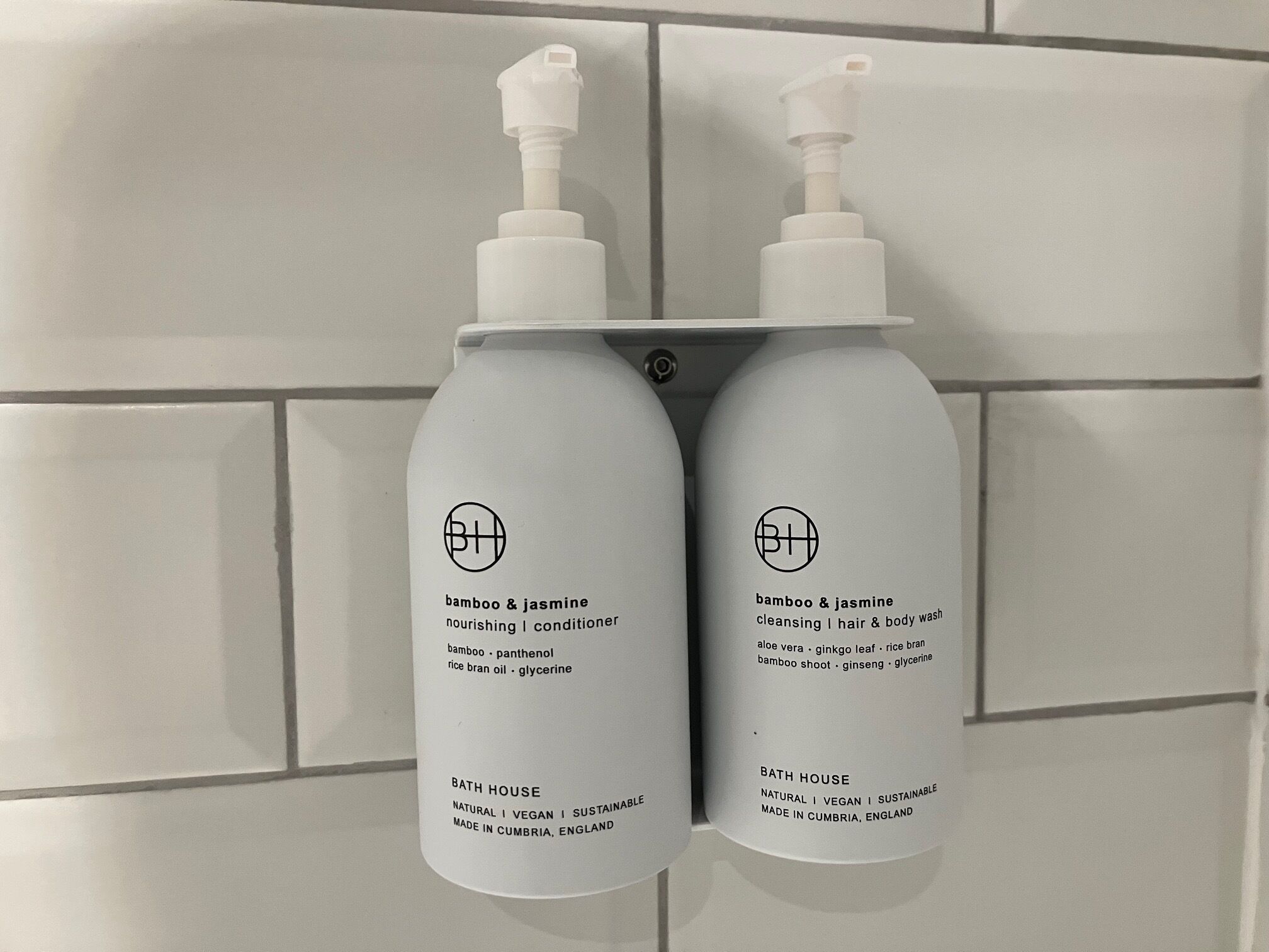 Two bottles of bath products labeled 'BATH HOUSE' with pump dispensers, placed on a tiled wall.