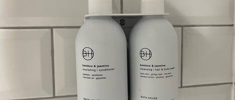 Two bottles of bath products labeled 'BATH HOUSE' with pump dispensers, placed on a tiled wall.