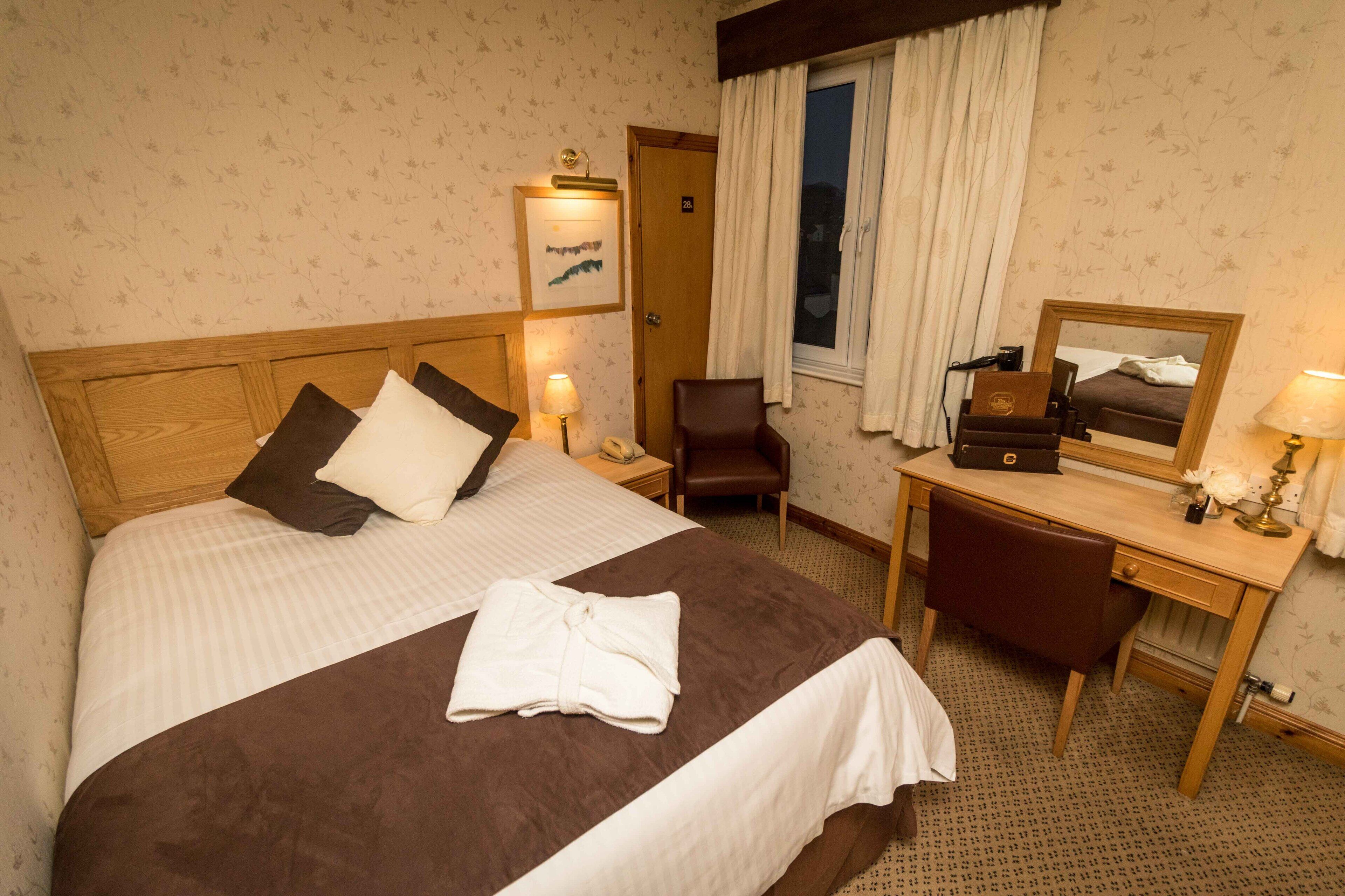 Una habitación de hotel con cama, escritorio, silla, espejo y puerta.