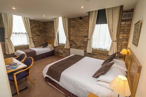 A hotel room with two beds, a desk with a chair, a lamp, and a window with curtains. - Washington Central Hotel and Sleepwell Inn (Workington)