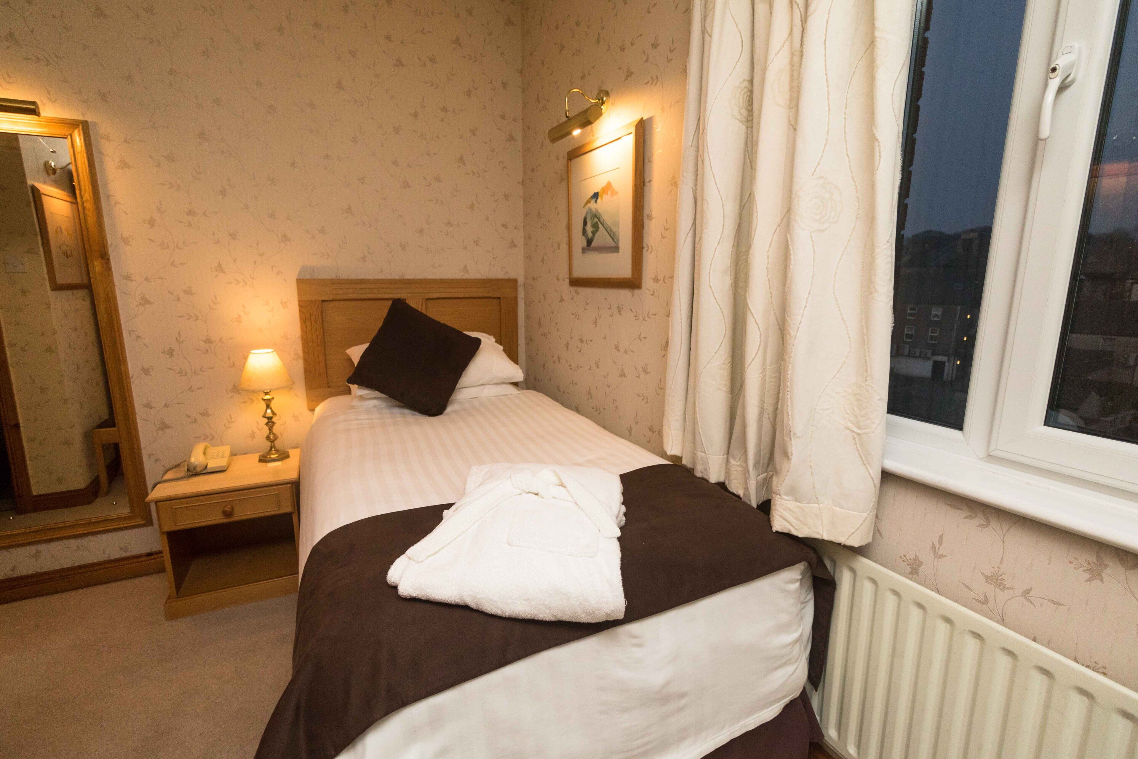 A neatly made bed with a white and brown comforter, a bedside lamp, a nightstand with a phone, and a framed picture on the wall.