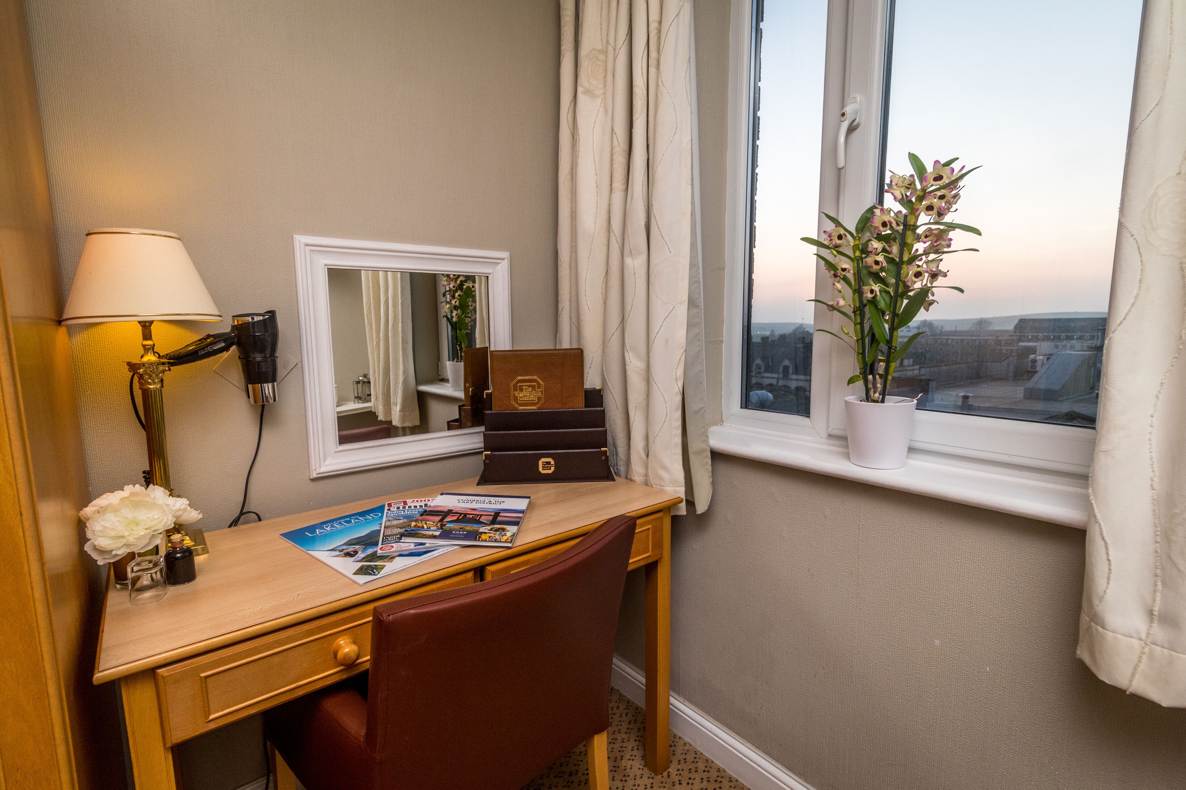 Habitación de hotel con escritorio, lámpara, espejo y ventana con vista a la ciudad.
