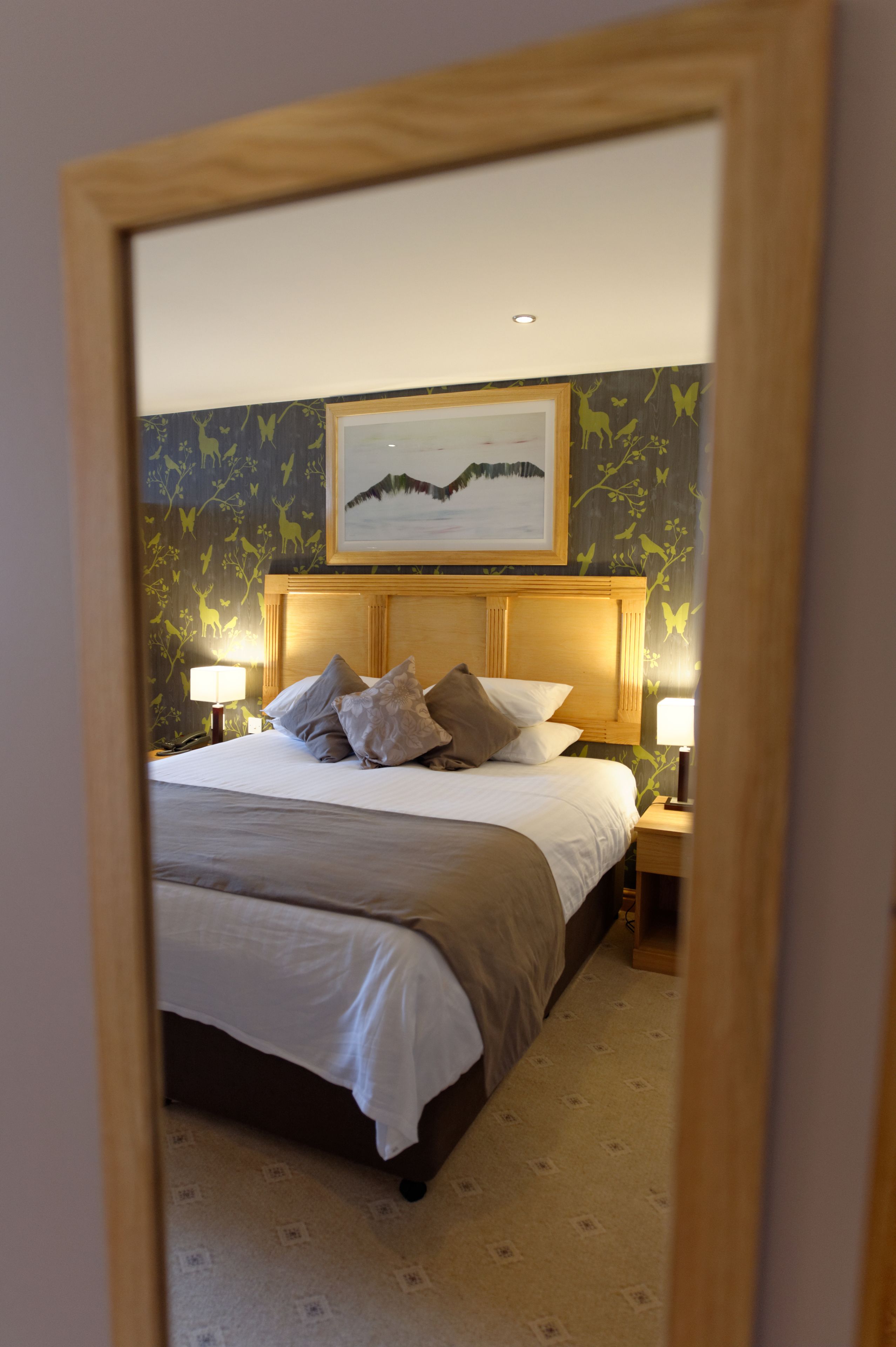 Ein Hotelzimmer mit einem großen Bett, zwei Nachttischen mit Lampen, einem gerahmten Bild über dem Bett und ornamentalem Wandpapier.