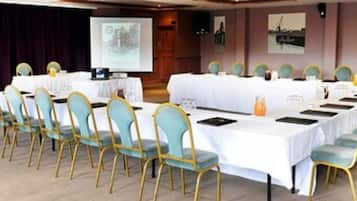 A conference room with long tables, chairs, a projector screen, and presentation boards.