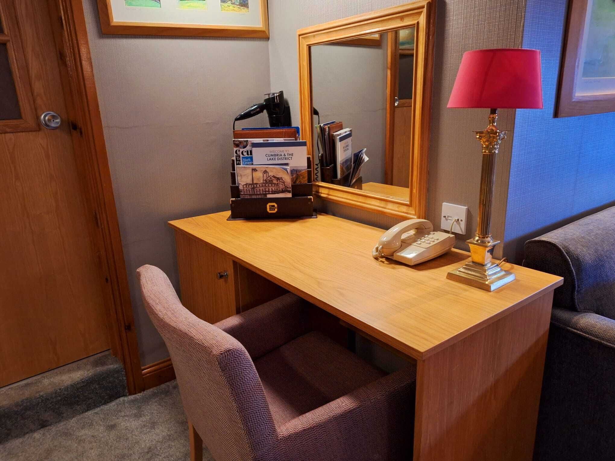 A wooden desk with a telephone, a lamp, and a magazine rack with brochures.