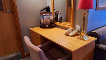 A wooden desk with a telephone, a lamp, and a magazine rack with brochures.