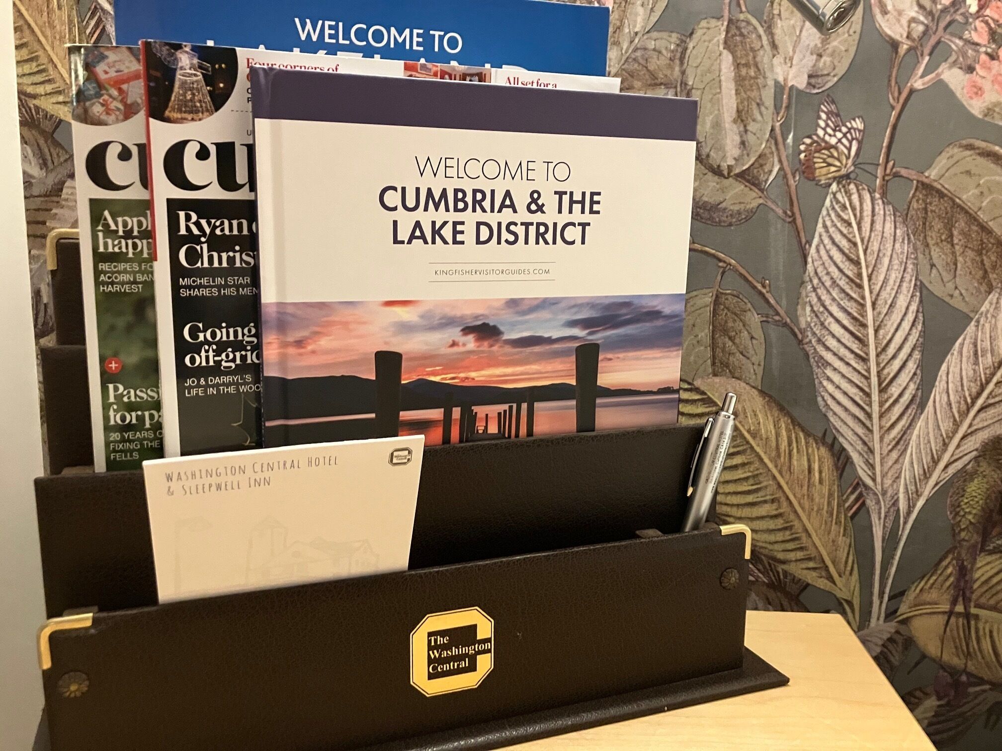 A welcome brochure for Cumbria & the Lake District, a pen, and a Washington Central Hotel & Sleepwell Inn brochure.