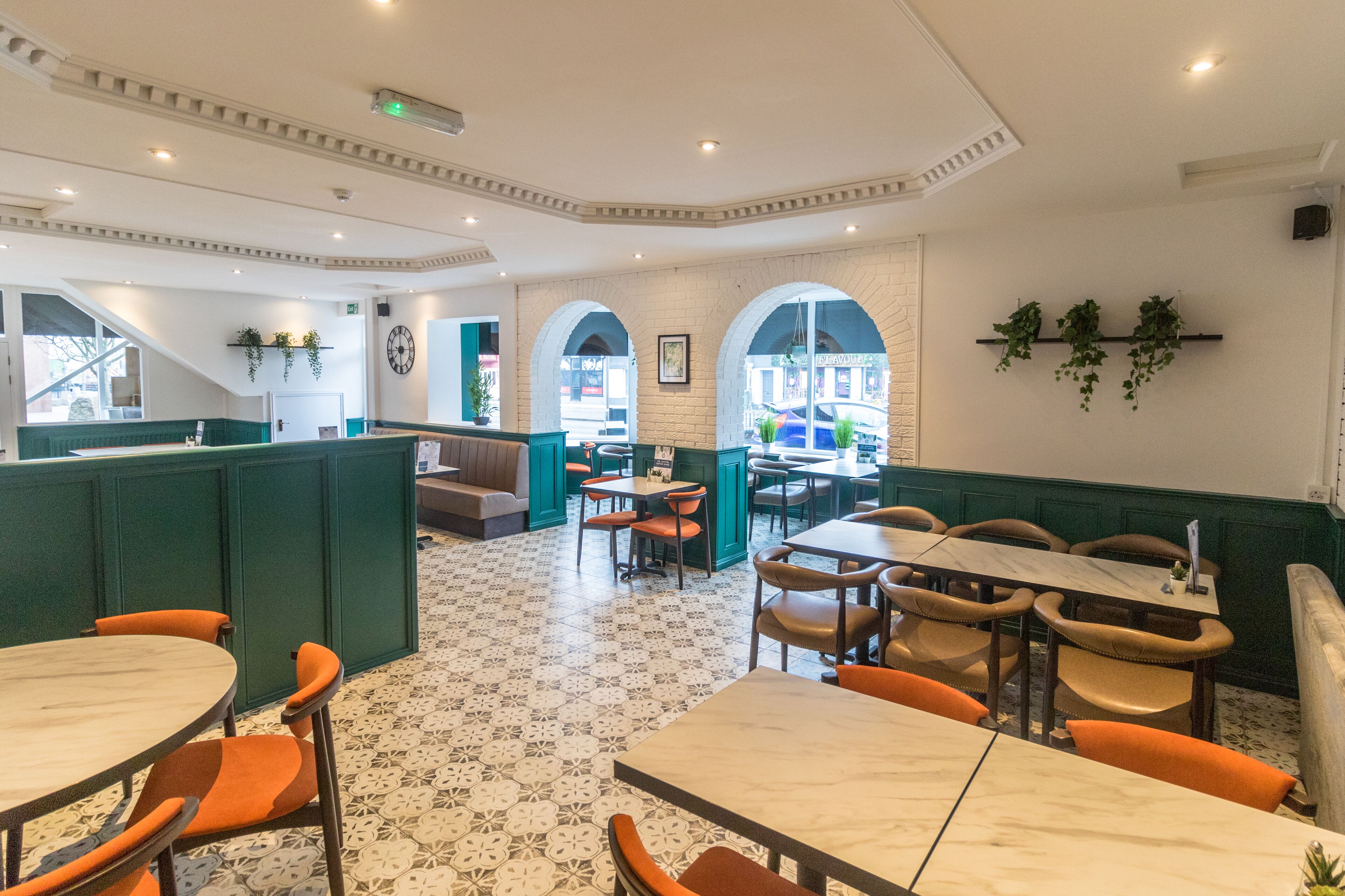 Ein Restaurant mit hohen Tischen und Sitzgelegenheiten in Form von Boxen, grünen gepolsterten Sitzflächen und einem gemusterten Boden.