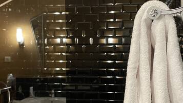 A modern bathroom with black tiled walls, a glass shower enclosure, and a white towel hanging on a metal rack.
