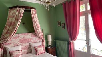 Une chambre à coucher avec un lit à baldaquin, un lustre, une fenêtre avec des rideaux rouges et un radiateur.