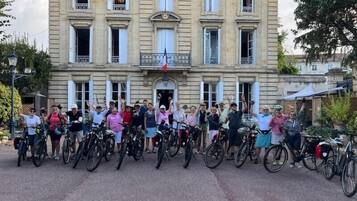 A group of people on bicycles in front of a large, historic building with multiple windows and a balcony.