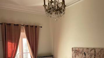 A bedroom with a large bed, a chandelier, a chair, a table, and a lamp.