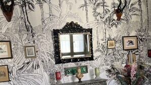 A room with a patterned wallpaper, a mirror, framed pictures, a vase with flowers, and a chandelier. - Chateau des Jacobins (Agen)