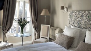 A hotel room with a large bed, a bedside table with a lamp, a chair, and a small table with a vase of flowers. - Chateau des Jacobins (Agen)