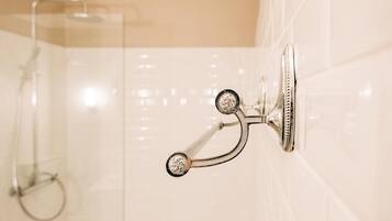 Une salle de bain dotée d’une pomme de douche fixée au mur et d’un espace de douche délimité par des parois en verre.
