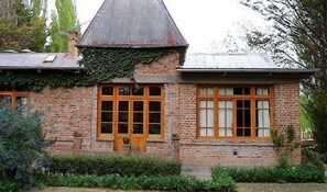 A brick house with a steeply pitched roof, large windows, and a small porch area. - La Casona del Rio (Trelew)