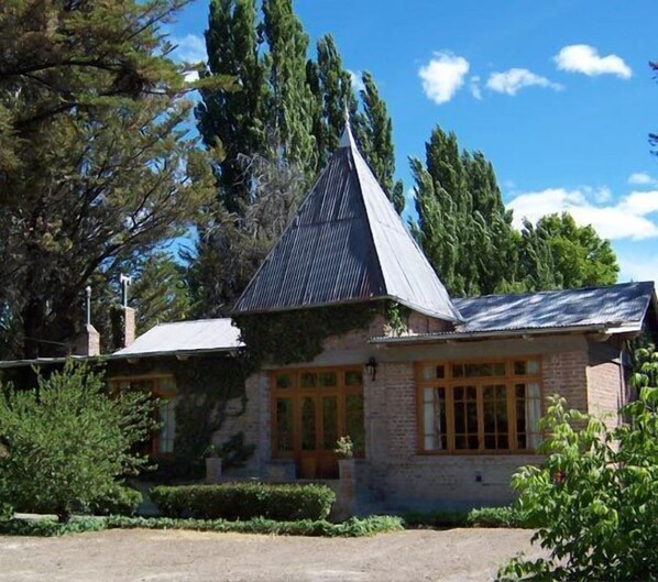 A building with a steeply pitched roof, stone walls, and large windows. - La Casona del Rio (Trelew)