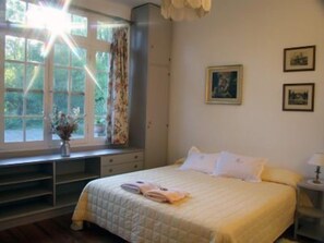 A bedroom with a bed, a window with curtains, a bedside table, and wall-mounted pictures. - La Casona del Rio (Trelew)
