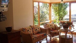 Un salon chaleureux, avec des meubles en osier, un téléviseur et une vue sur la verdure environnante.