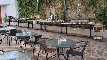 Eine Terrasse im Freien mit runden Tischen und Stühlen, einem Büfett und einer mit Grünpflanzen bewachsenen Wand.
