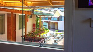 Vista attraverso una finestra che mostra un edificio con soffitto in legno, un'area con posti a sedere all'aperto e una porta ben visibile.