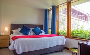 A bed with a red blanket, two blue pillows, a white headboard, and a nightstand with a lamp.