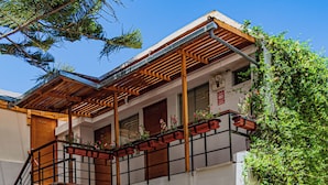 Un edificio con una scala in pietra che conduce a un balcone in legno, circondato da piante in vaso e un cielo azzurro intenso.
