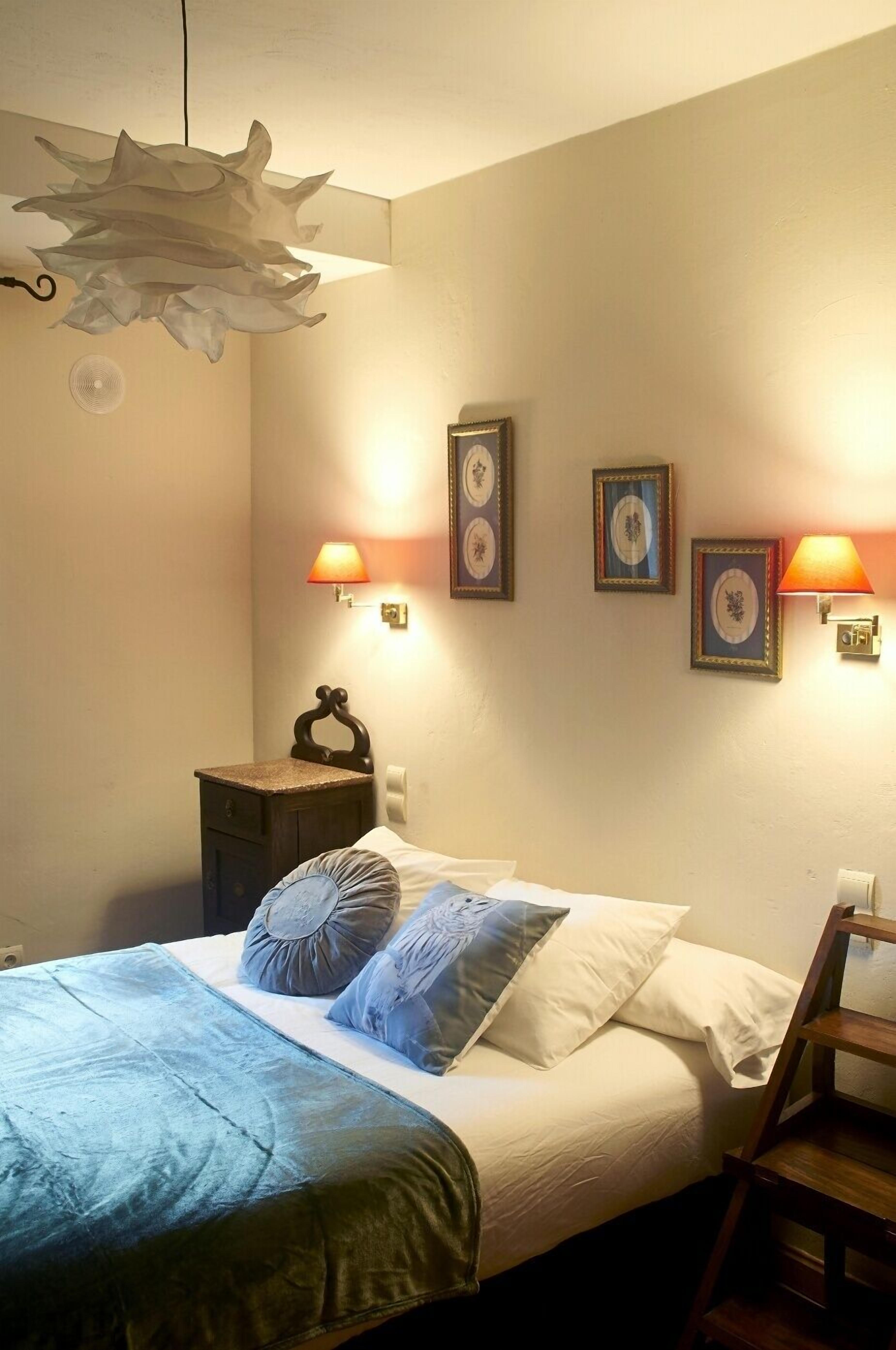 A bedroom with a bed, bedside lamps, a nightstand, and wall-mounted picture frames.