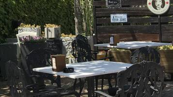 An outdoor seating area with metal chairs and tables, surrounded by greenery and a wooden fence.