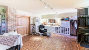 A compact kitchen with a central island, a dining area with a table and chairs, and a brick wall with a door. - El Torreón de Navacerrada (Navacerrada)