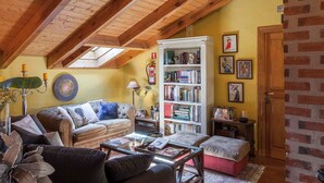 A cozy loft-style living room with a high wooden ceiling, a large bookshelf, and a comfortable seating area with a sofa and ottoman. - El Torreón de Navacerrada (Navacerrada)