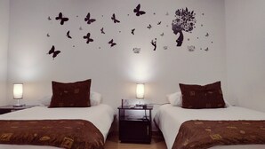 A hotel room with two beds, each with brown bedding and pillows, a nightstand with a lamp, and a wall decoration of butterflies and a tree. - Hotel Confort Bogotá (Bogotá)