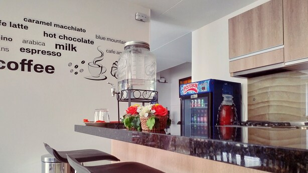 A modern kitchen with a coffee station, a Postobon refrigerator, and a wall with coffee-related words. - Hotel Confort Bogotá (Bogotá)