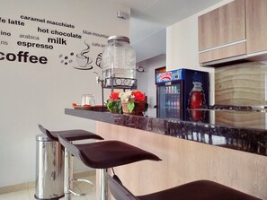 A modern kitchen with a coffee station, a Postobon refrigerator, and a wall with coffee-related words. - Hotel Confort Bogotá (Bogotá)