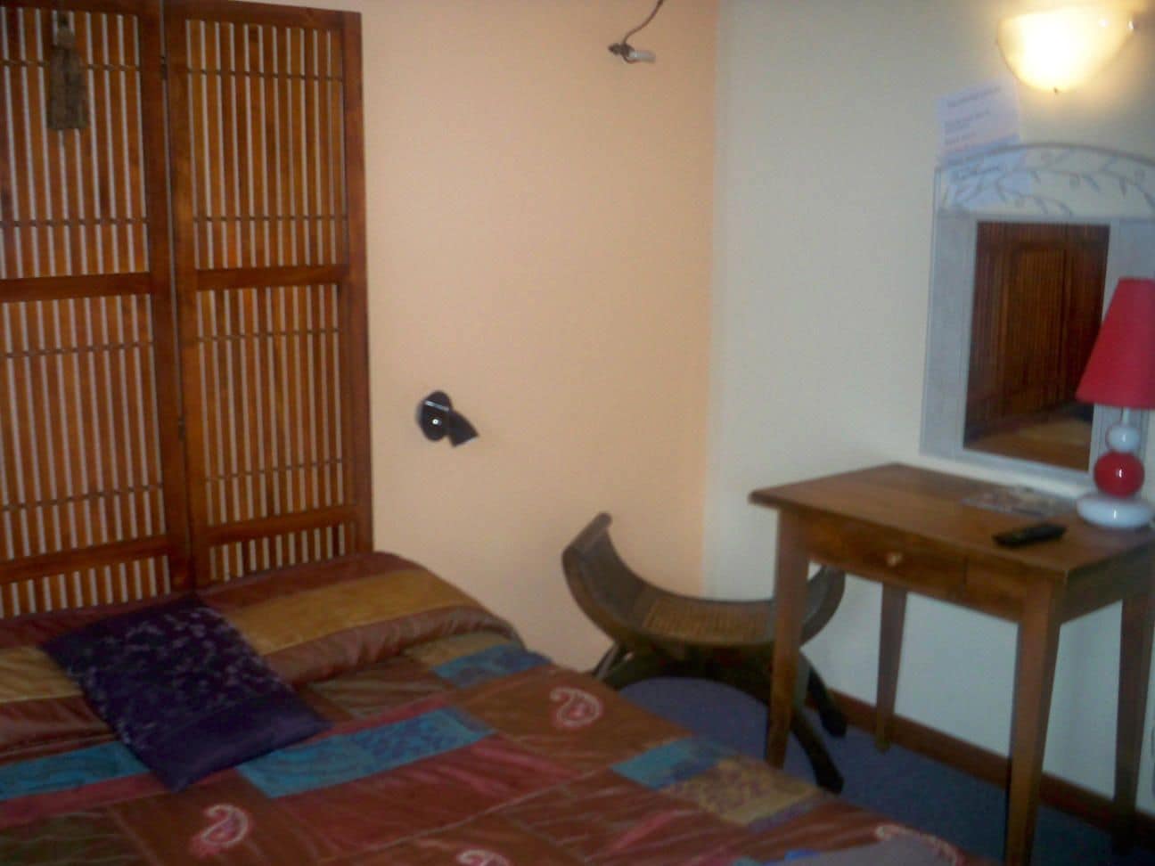 A room with a bed, a wooden desk, a chair, and a lamp.